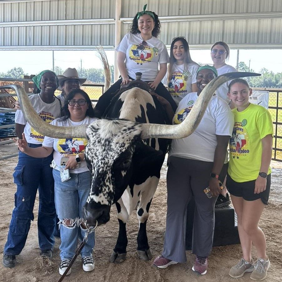 Group posing with a longhorn steer under a barn roof, wearing matching T-shirts and smiling.