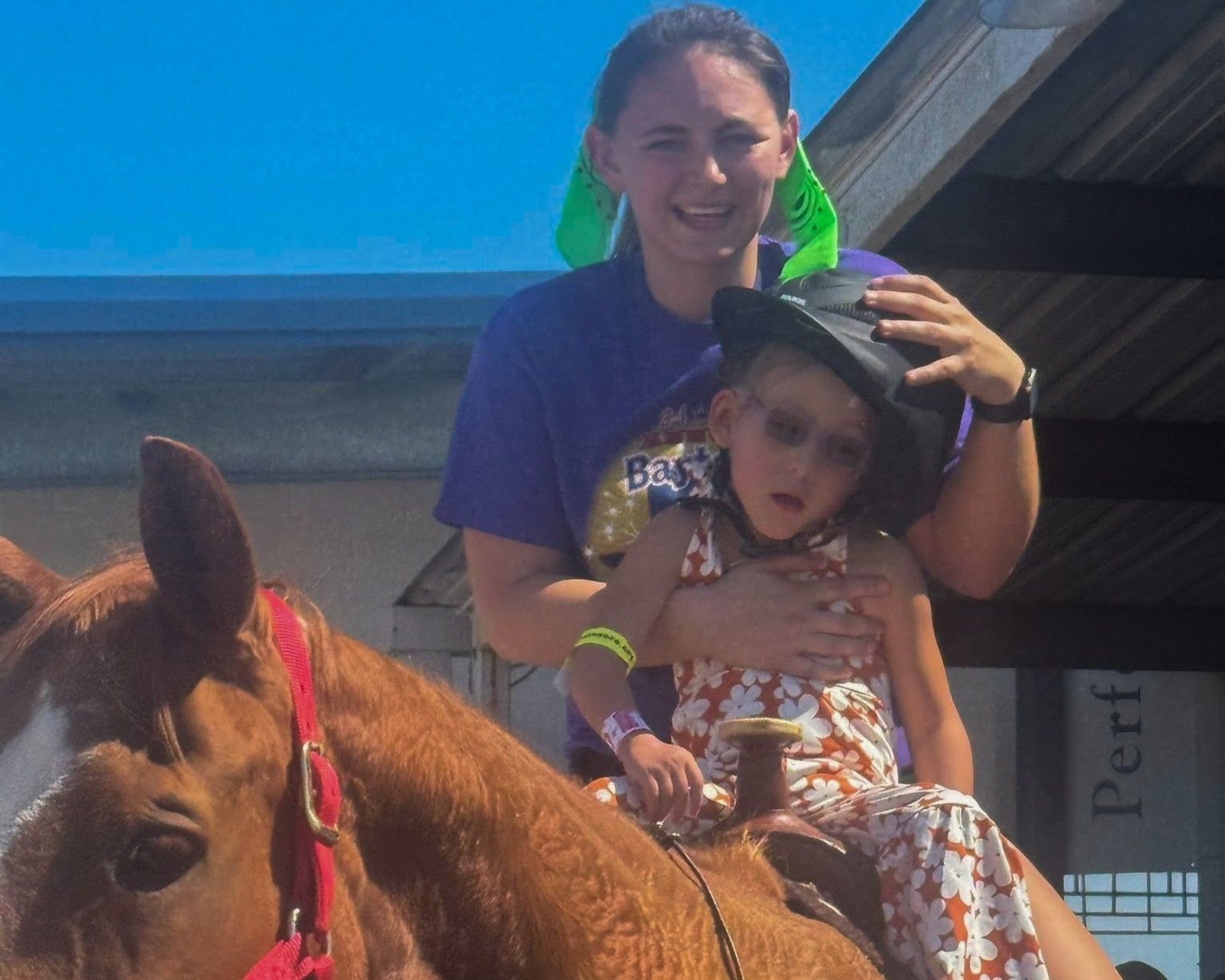 Smiling adult with child on a horse, outdoors in bright sun.