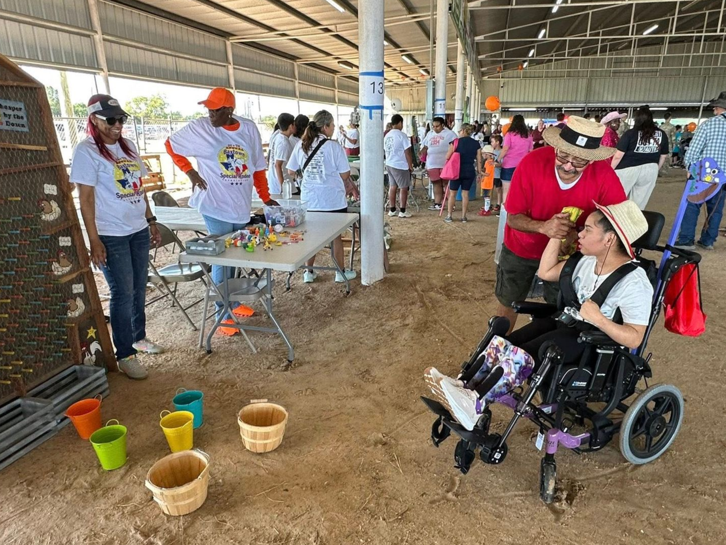 People at an indoor fair with baskets, cups, and a woman in a wheelchair holding a baby.