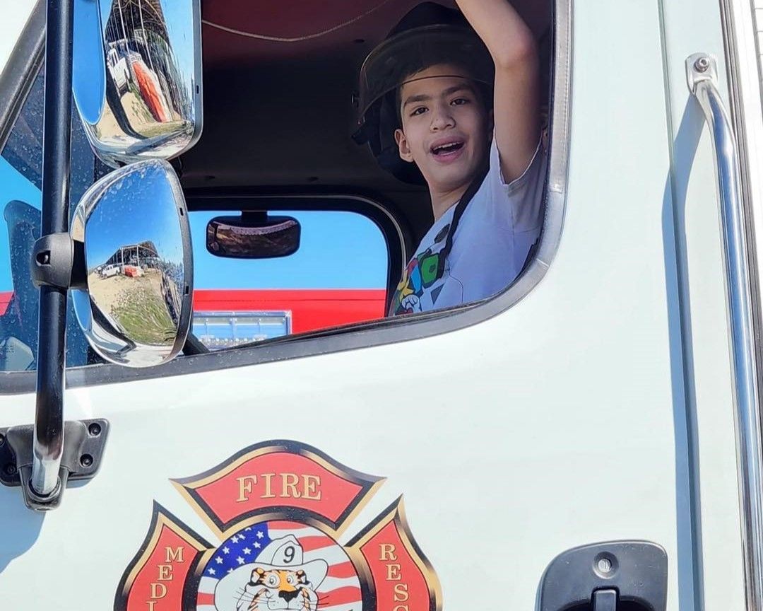 Smiling child waving from a fire truck window with a fire department emblem visible