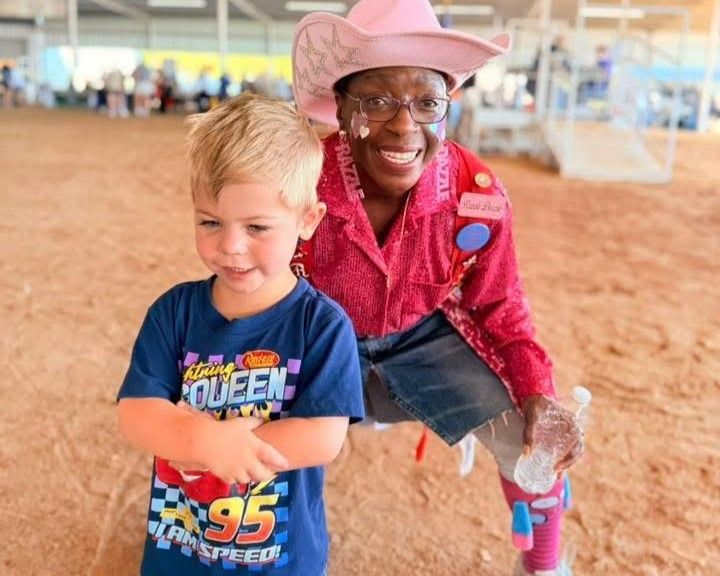 Two smiling children in cowboy hats at a sandy outdoor event, one in a blue shirt and one in pink.
