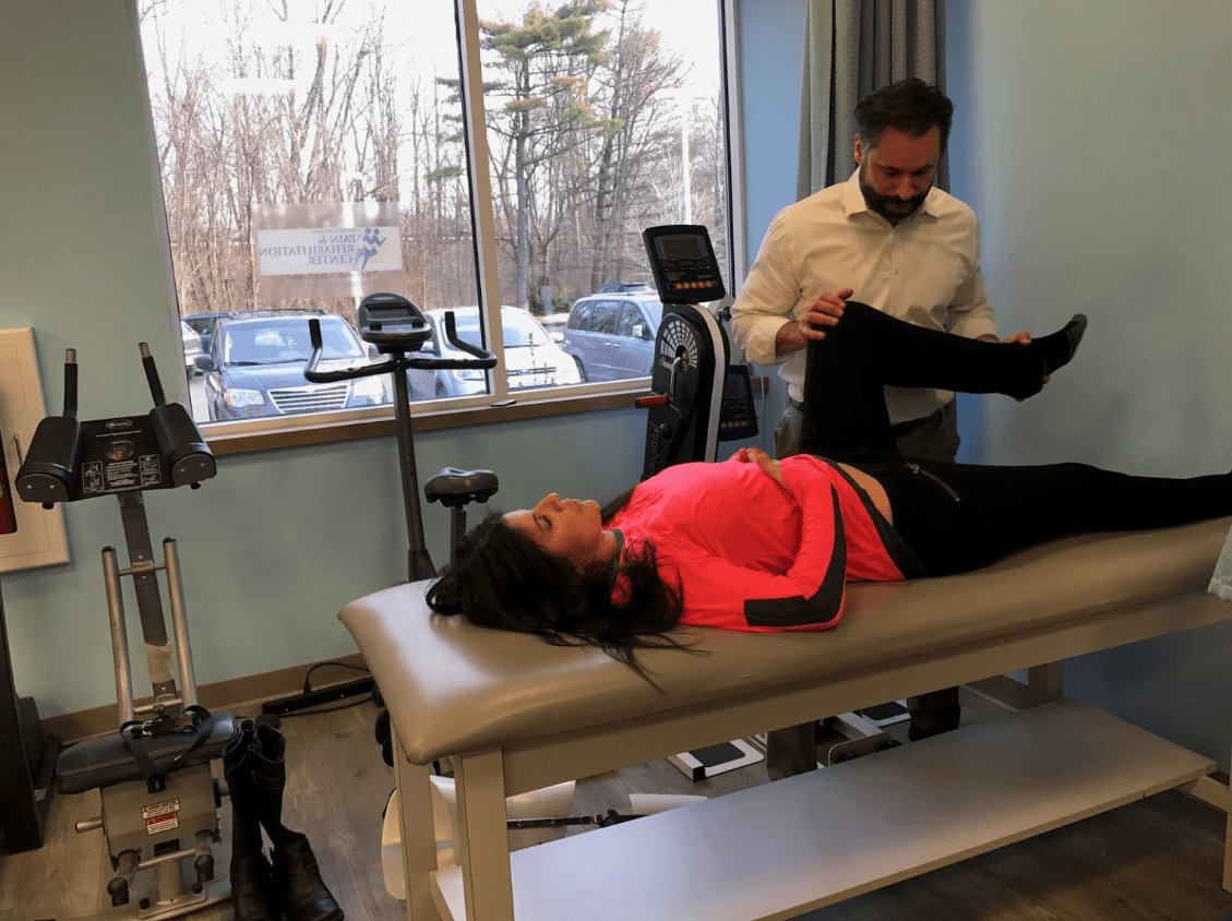 Physical therapist assisting a patient with a leg stretch on a treatment table.
