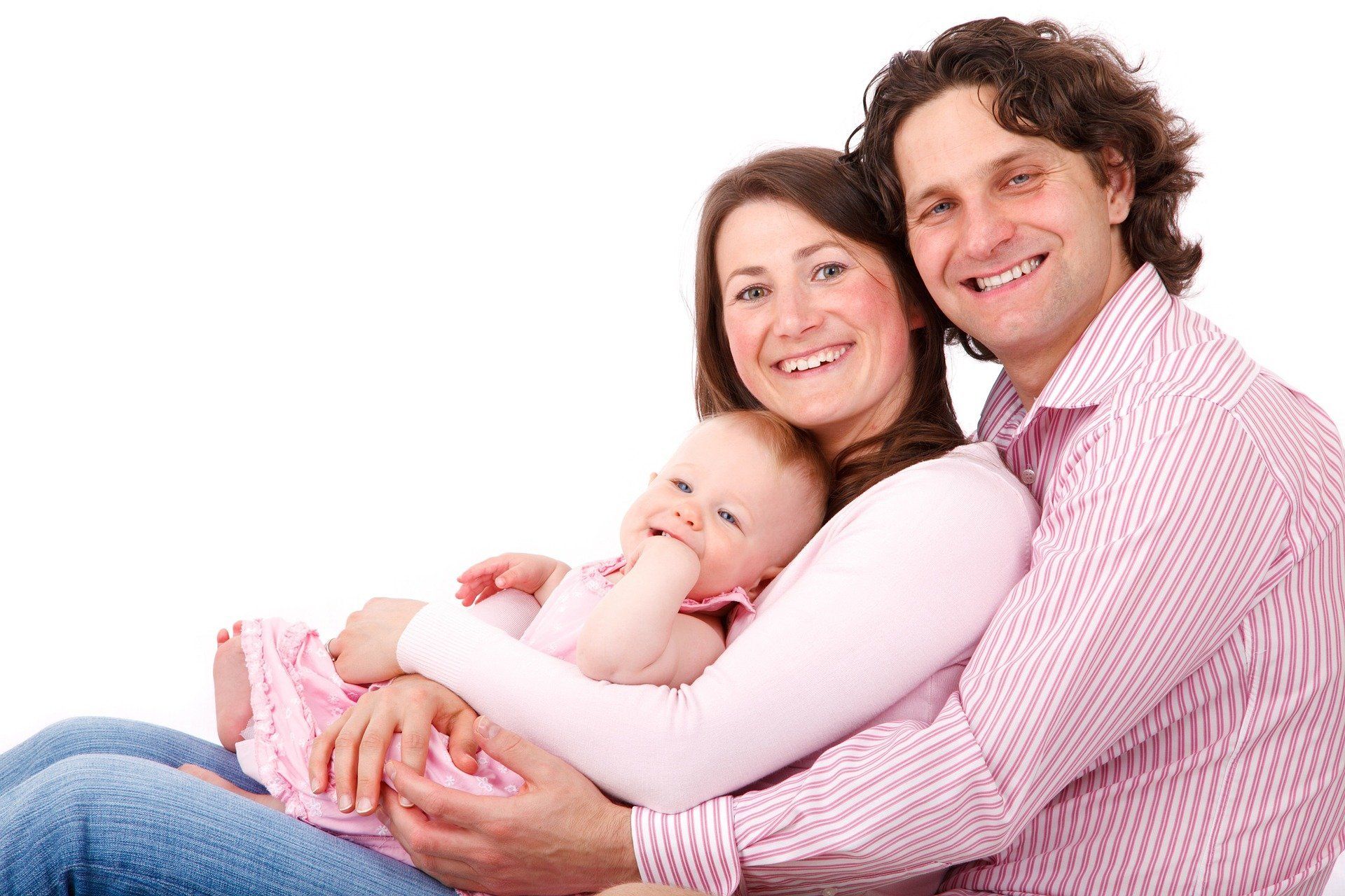 Smiling couple holding a baby while sitting together on a white background.
