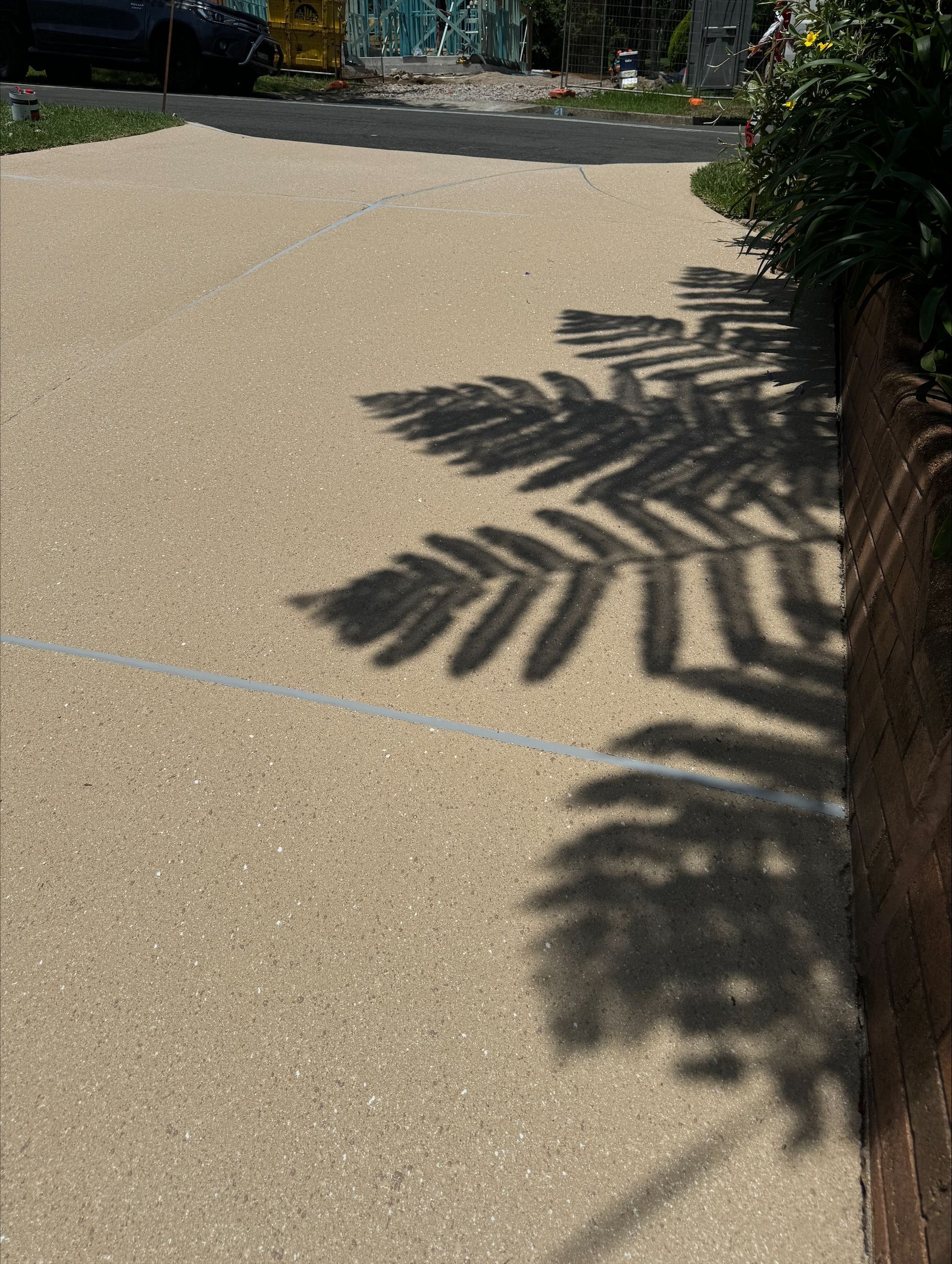 A Man Is Standing in A Driveway Next to A Fence — Illawarra Resurfacing Pty Ltd in Thirroul, NSW