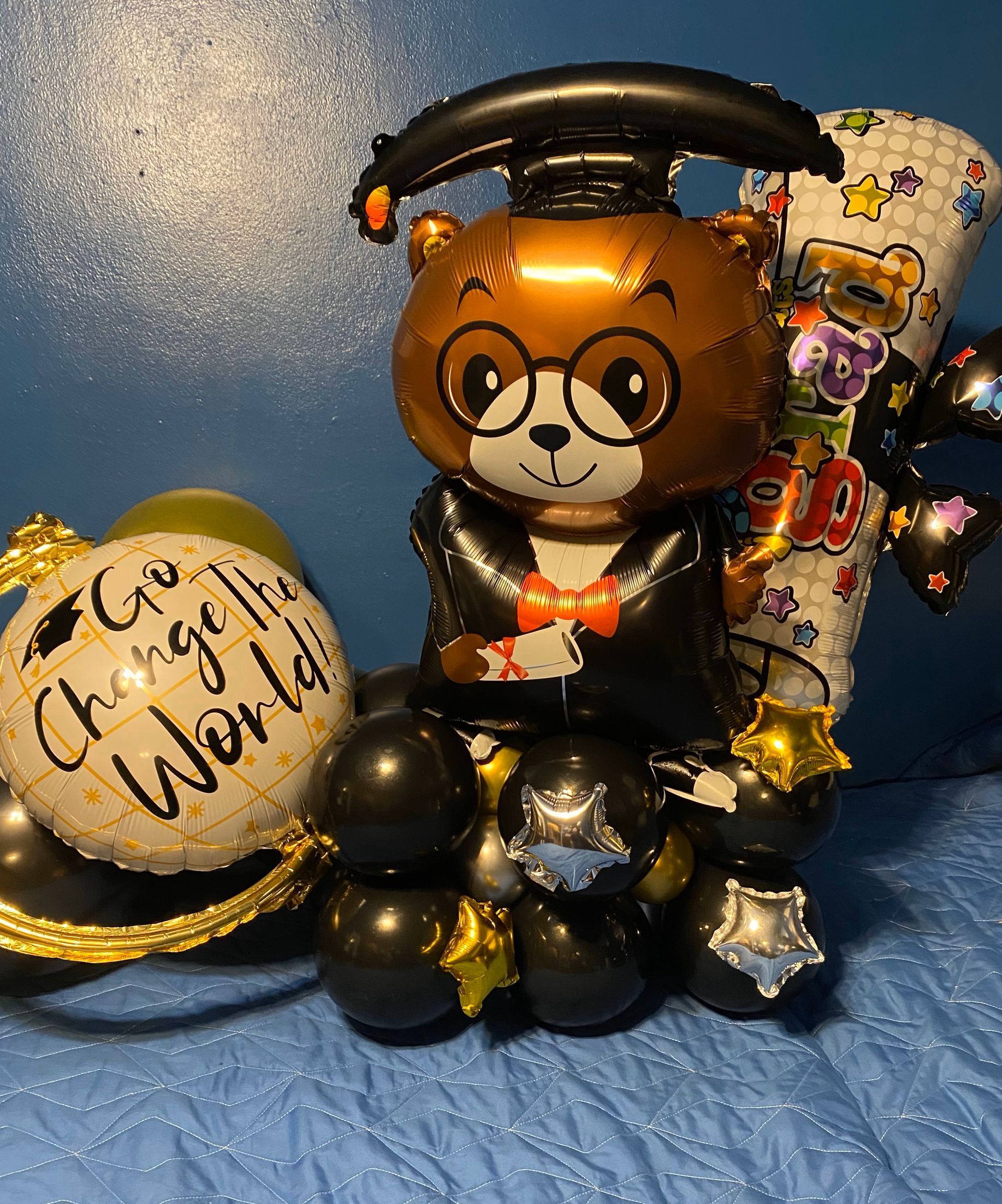 A teddy bear in a graduation cap and go change the world balloon.