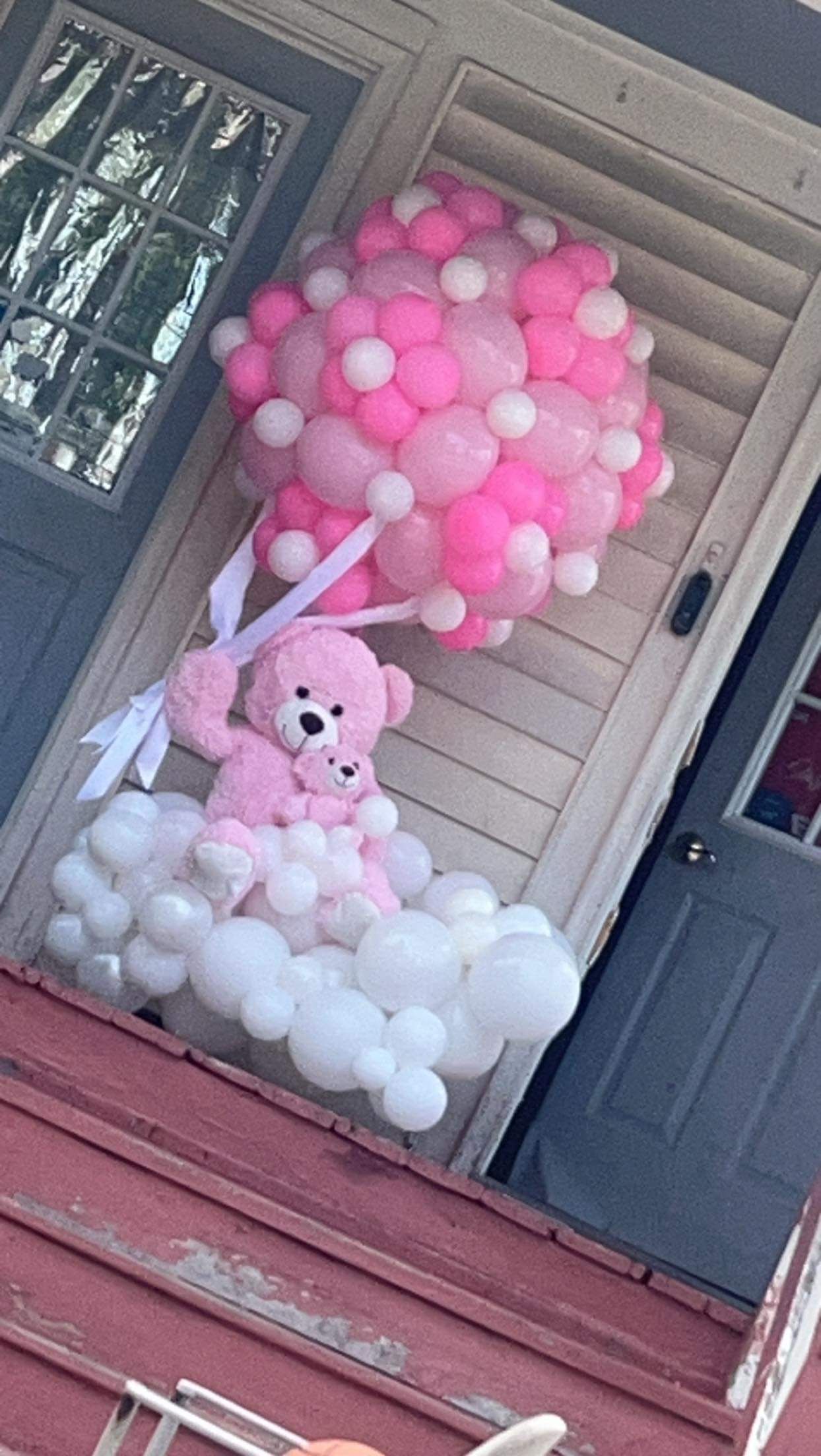 A pink teddy bear is sitting on top of a bunch of pink and white balloons.