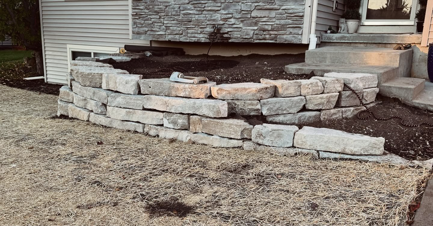 A curved stone retaining wall surrounding a garden bed near a house entrance.