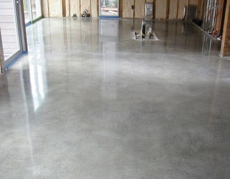 Polished concrete floor in a room under construction, reflecting sunlight.