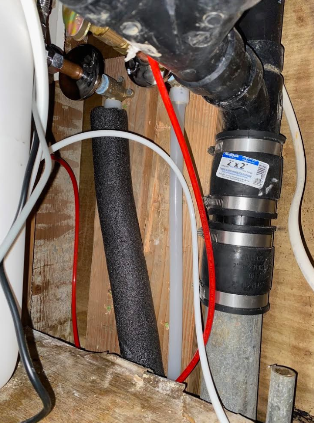 Tight view of plumbing pipes, hoses, and valves in a utility space with red and black tubing