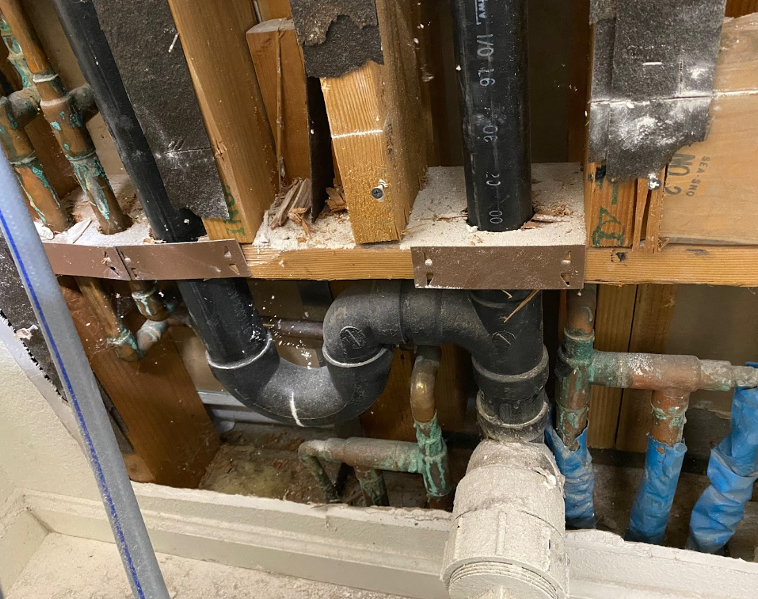 Exposed plumbing and pipes inside a wall, with black and blue insulated lines and wooden framing.