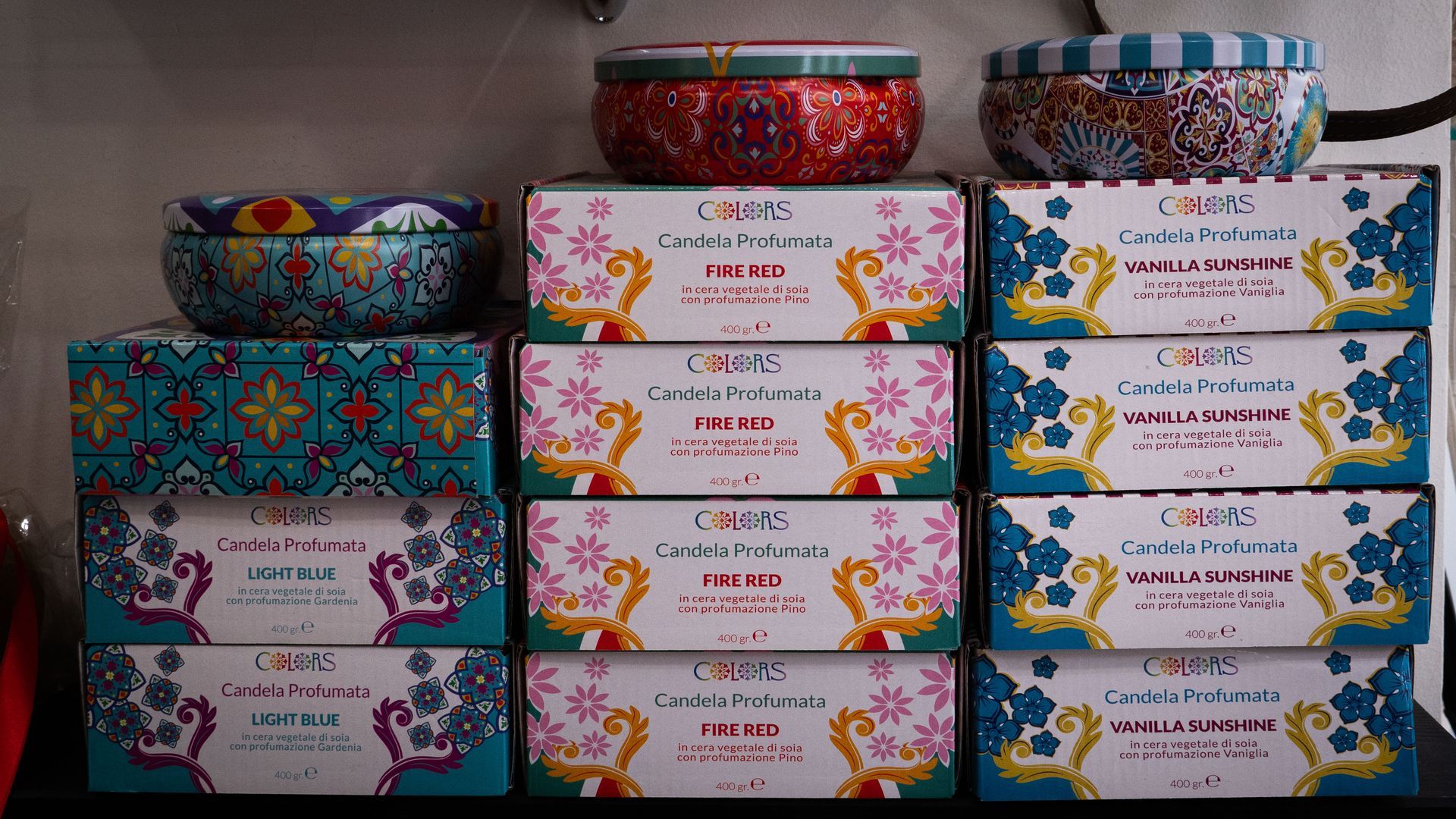 Candele impilate sullo scaffale: varie scatole di latta colorate e candele in scatola.