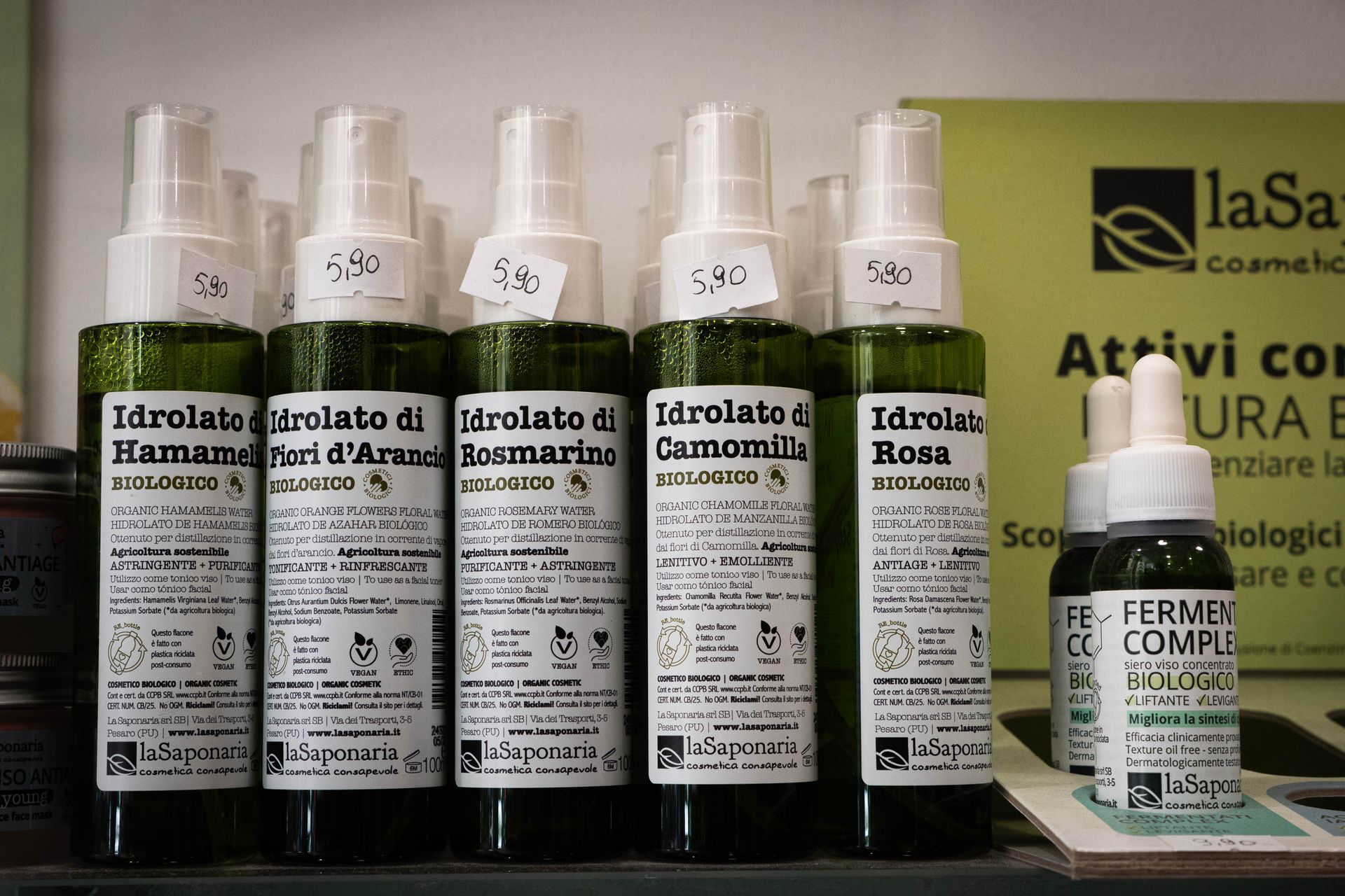 Flaconi di prodotti cosmetici su uno scaffale. Le etichette riportano nomi, prezzi e il logo del marchio in italiano.