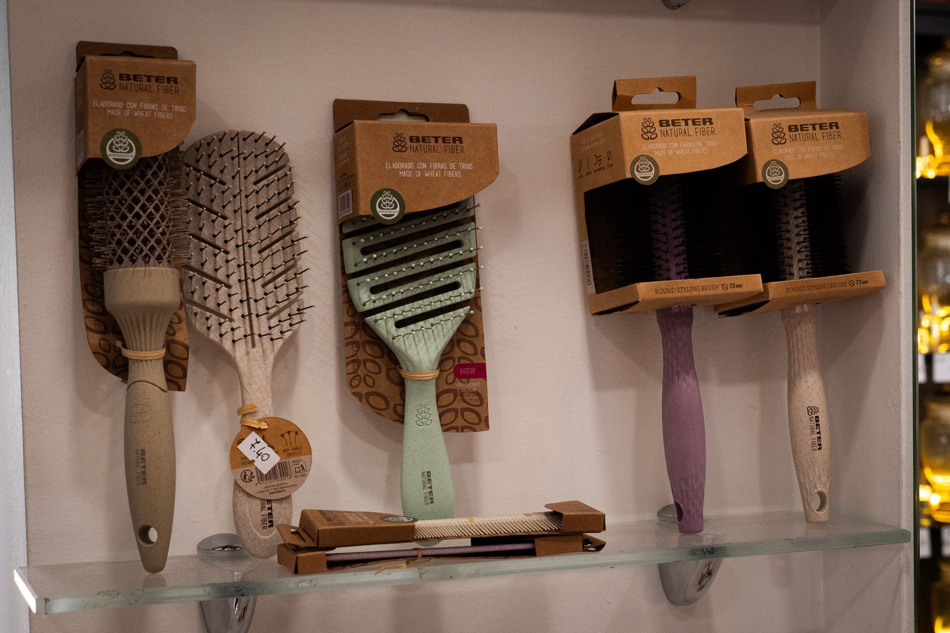 Spazzole per capelli esposte su uno scaffale. Varie forme e colori, con manici in legno e confezione in cartone.