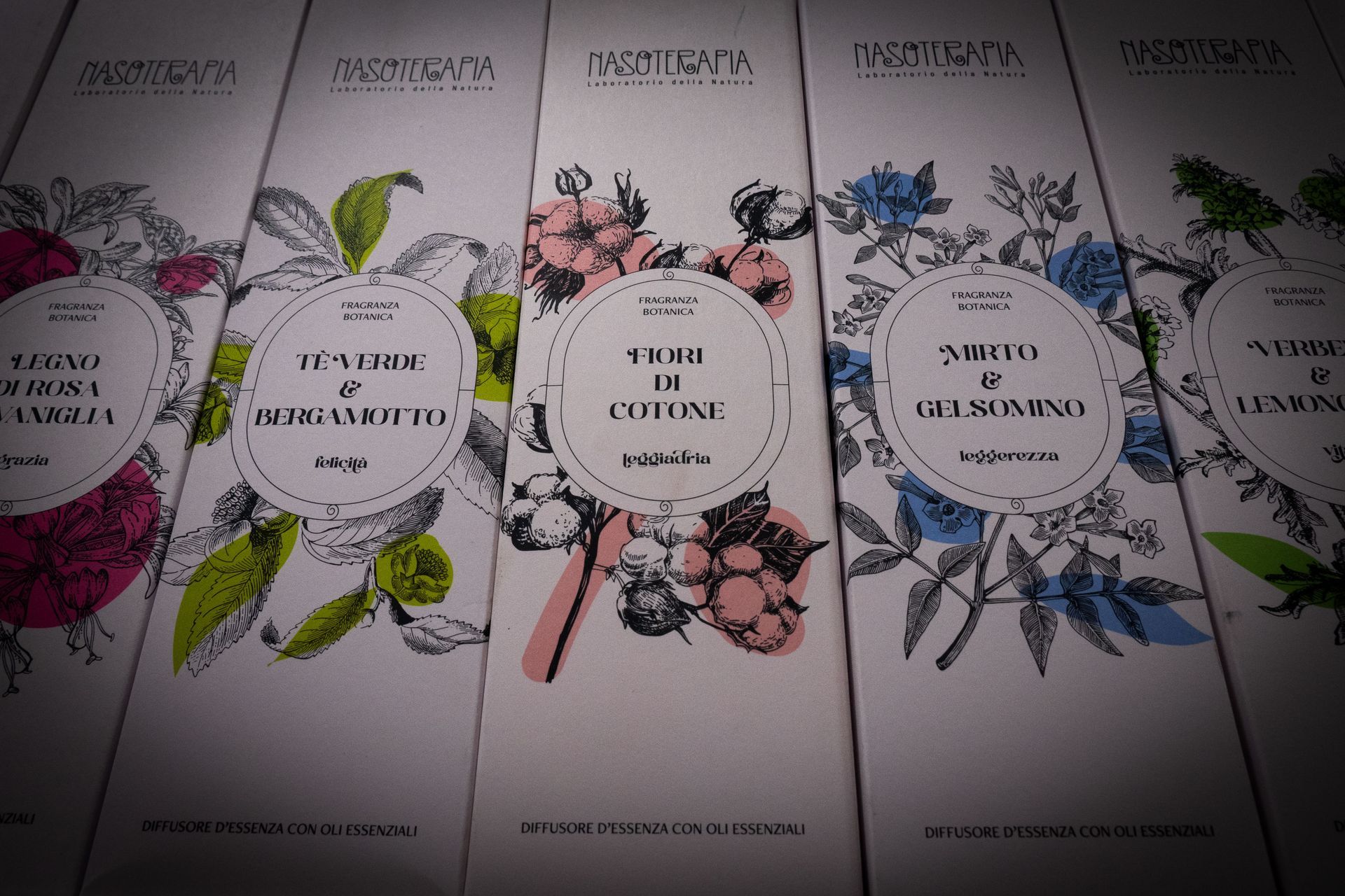 Primo piano di cinque scatole bianche con illustrazioni botaniche ed etichette di testo in vari colori.