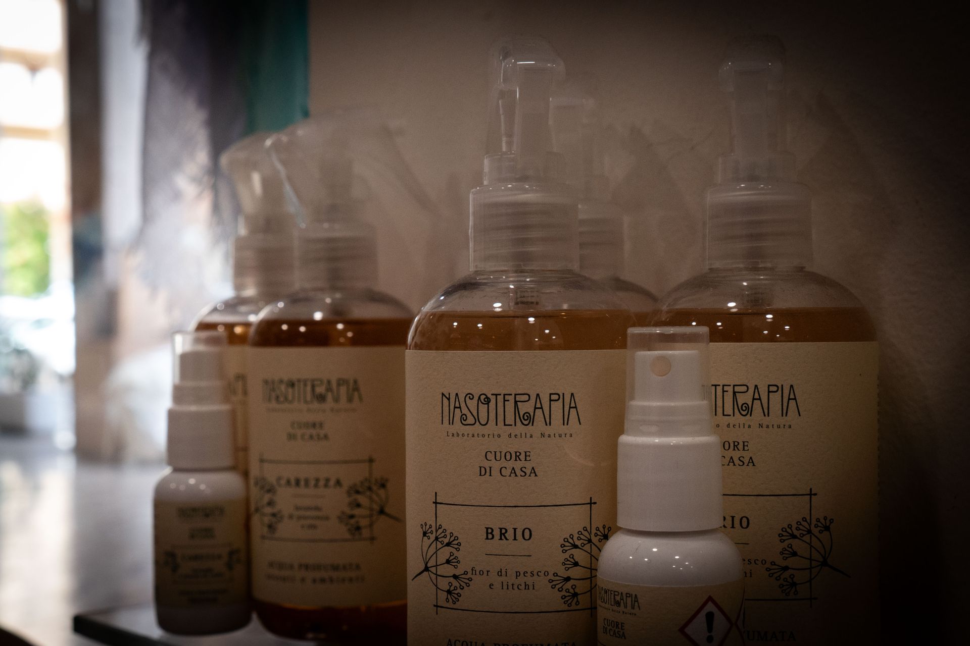 Flaconi di vari prodotti per la cura dei capelli su uno scaffale, illuminati dalla luce naturale.