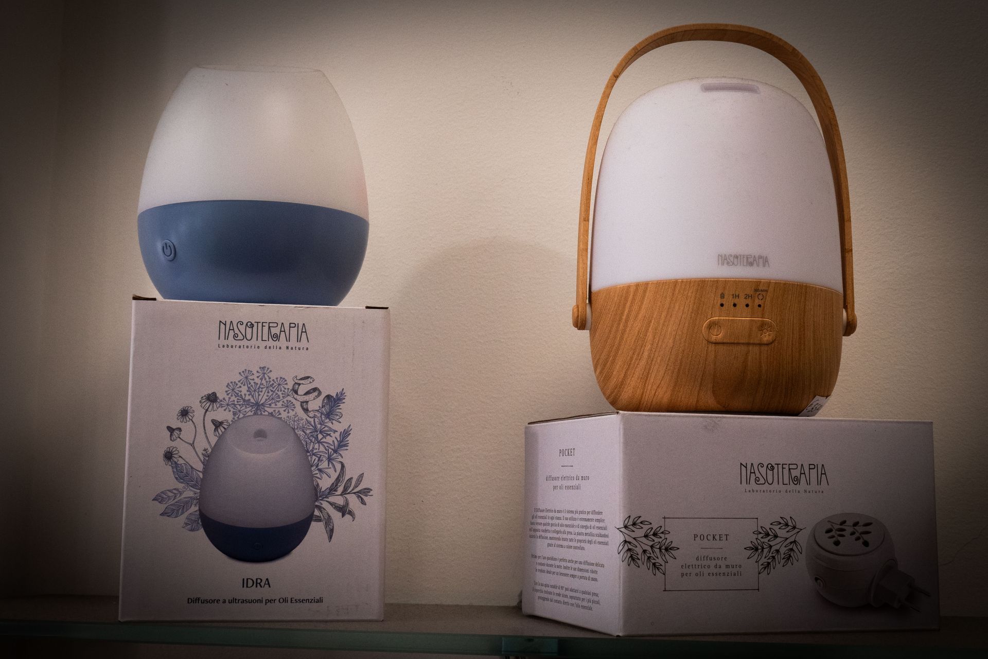Su uno scaffale sono ubicati due diffusori di aromi in scatole, uno blu e uno con manico in legno.