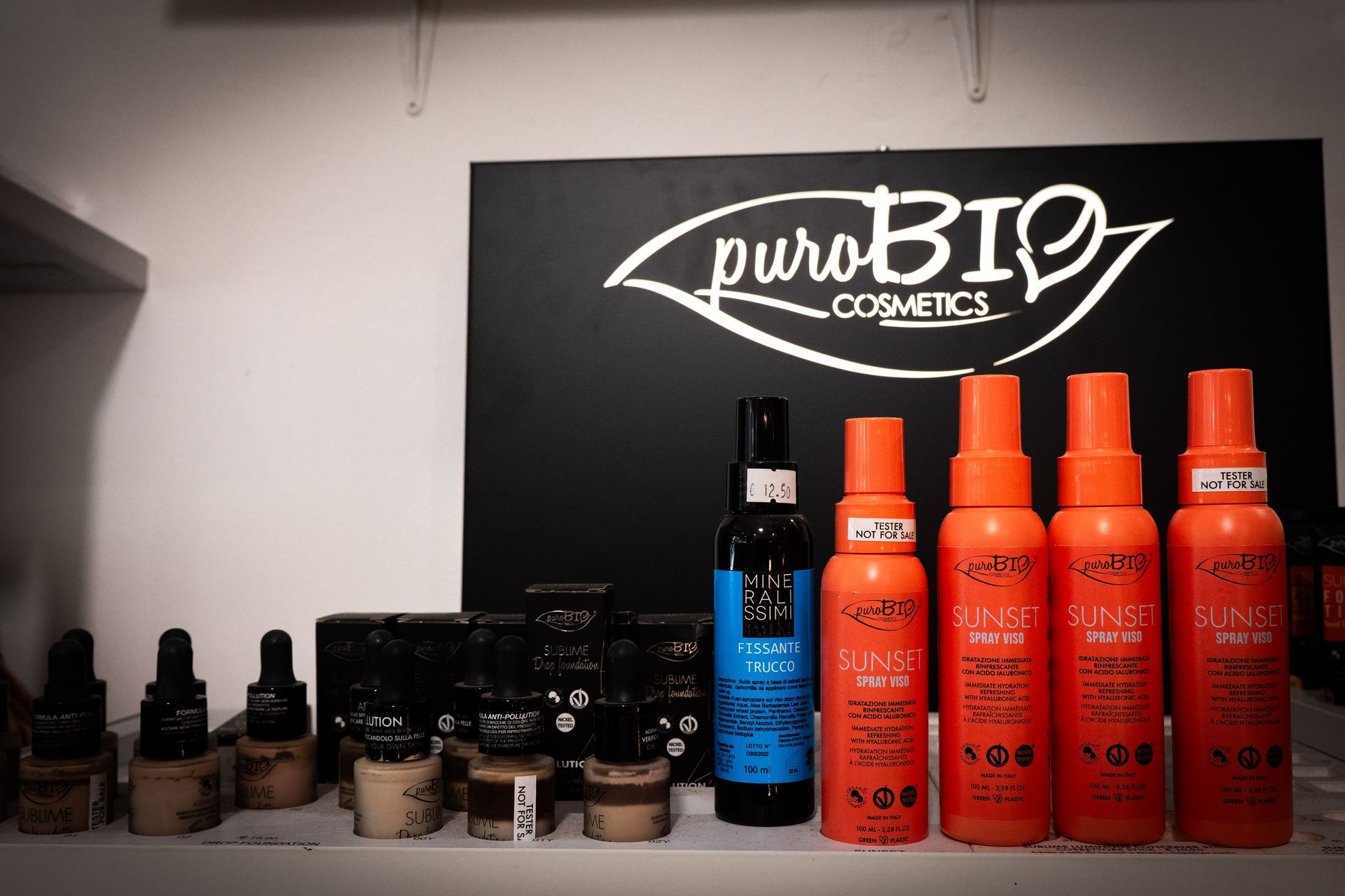 Espositore per cosmetici con flaconi arancioni e marroni sotto il logo