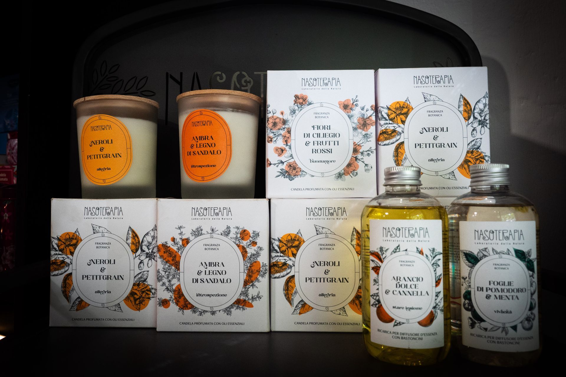 Varie candele profumate e prodotti da bagno con motivi floreali e dettagli arancioni.