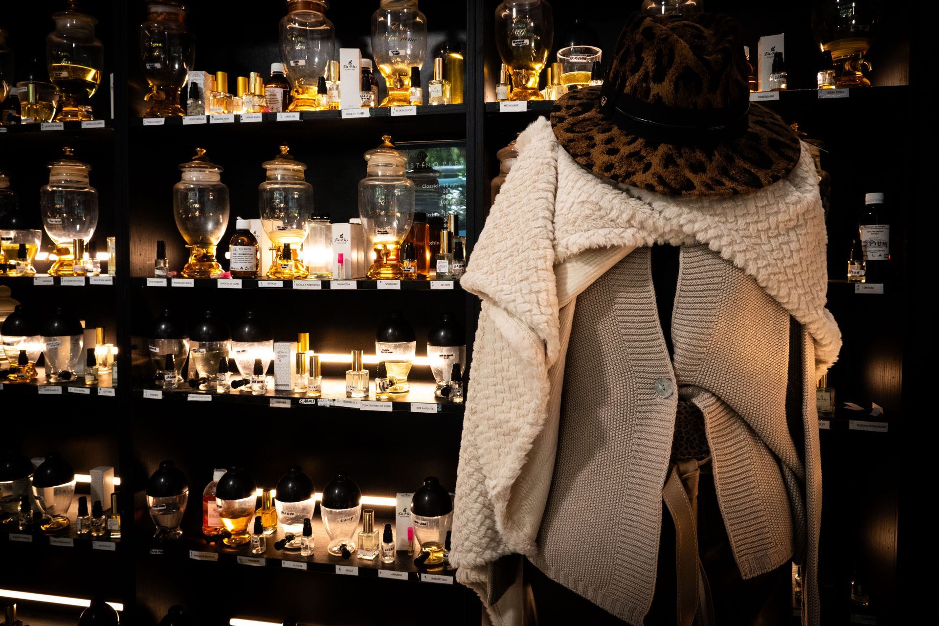 Un cappotto con un cappello leopardato esposto davanti a scaffali pieni di bottiglie e barattoli di profumo.