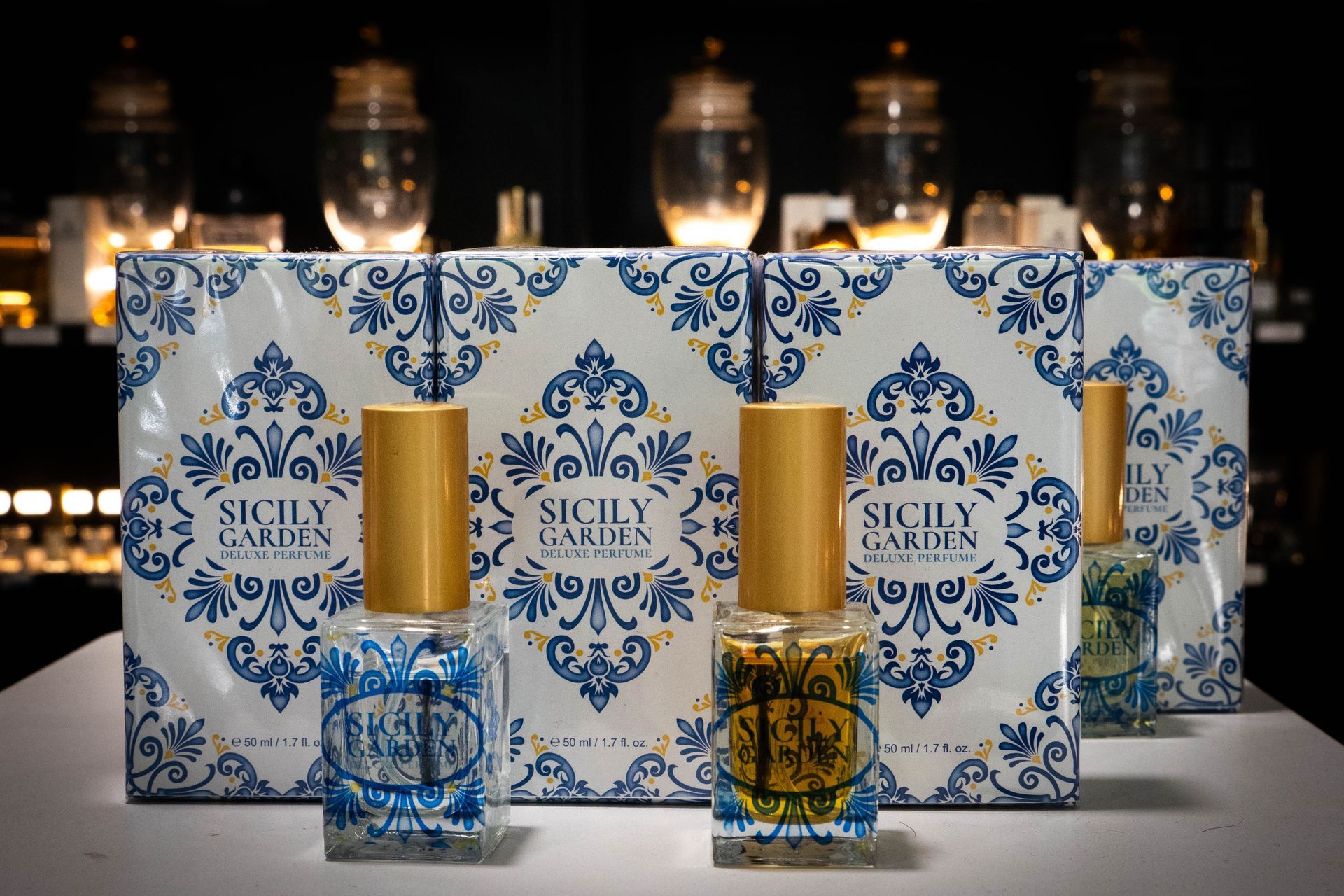 Bottiglie di profumo davanti a scatole con motivi floreali blu e bianchi; barattoli sullo sfondo.