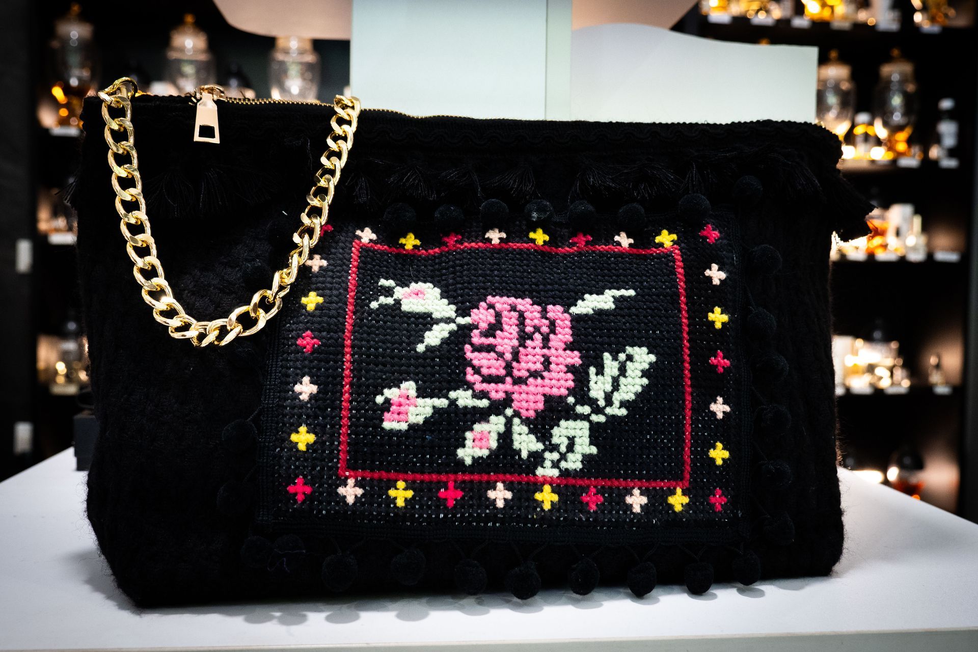 Pochette nera con tracolla a catena dorata, motivo ricamato a forma di rosa nei colori rosa, verde e rosso.