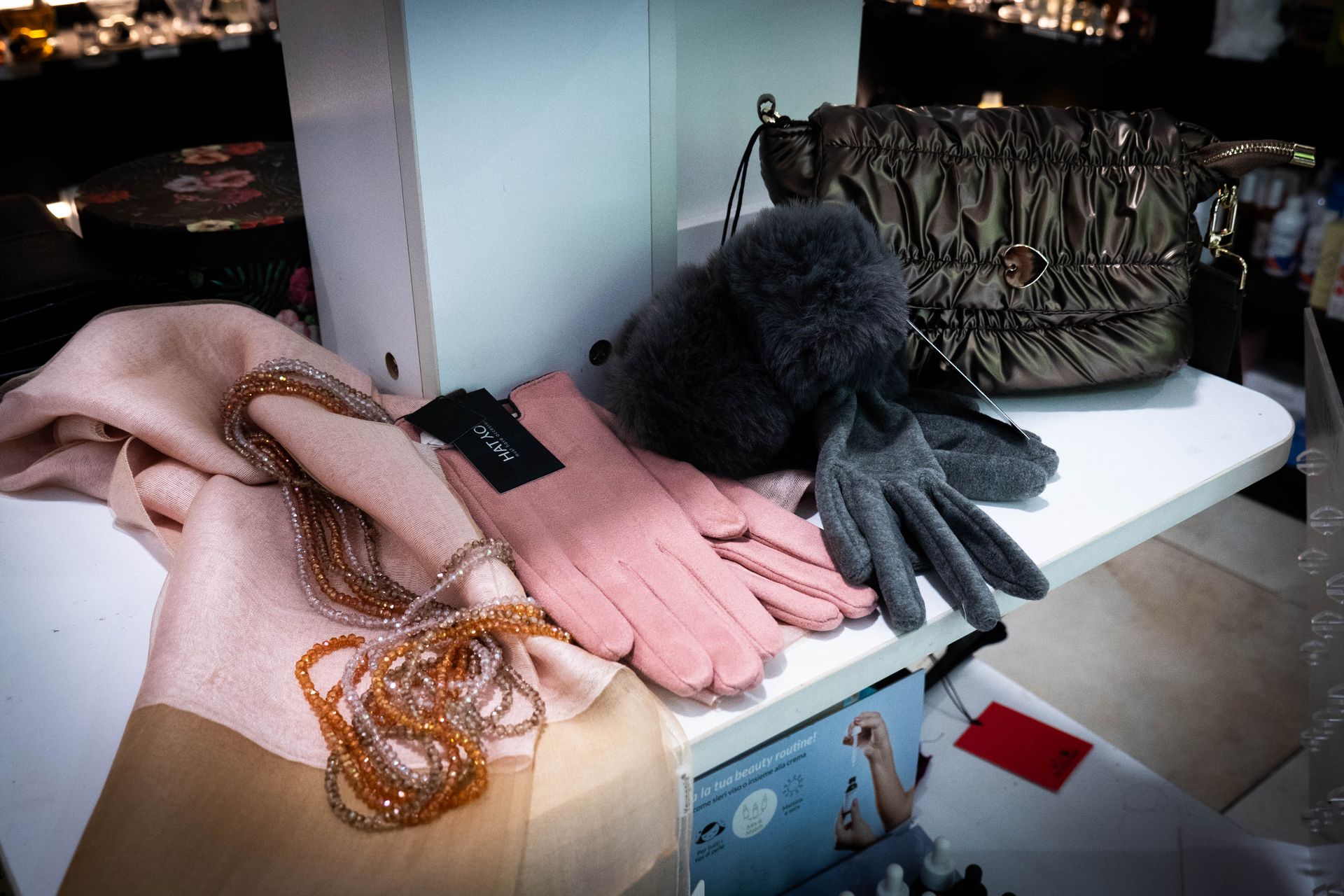 Guanti rosa, sciarpa, gioielli, cappello di pelliccia e una borsa marrone su uno scaffale.