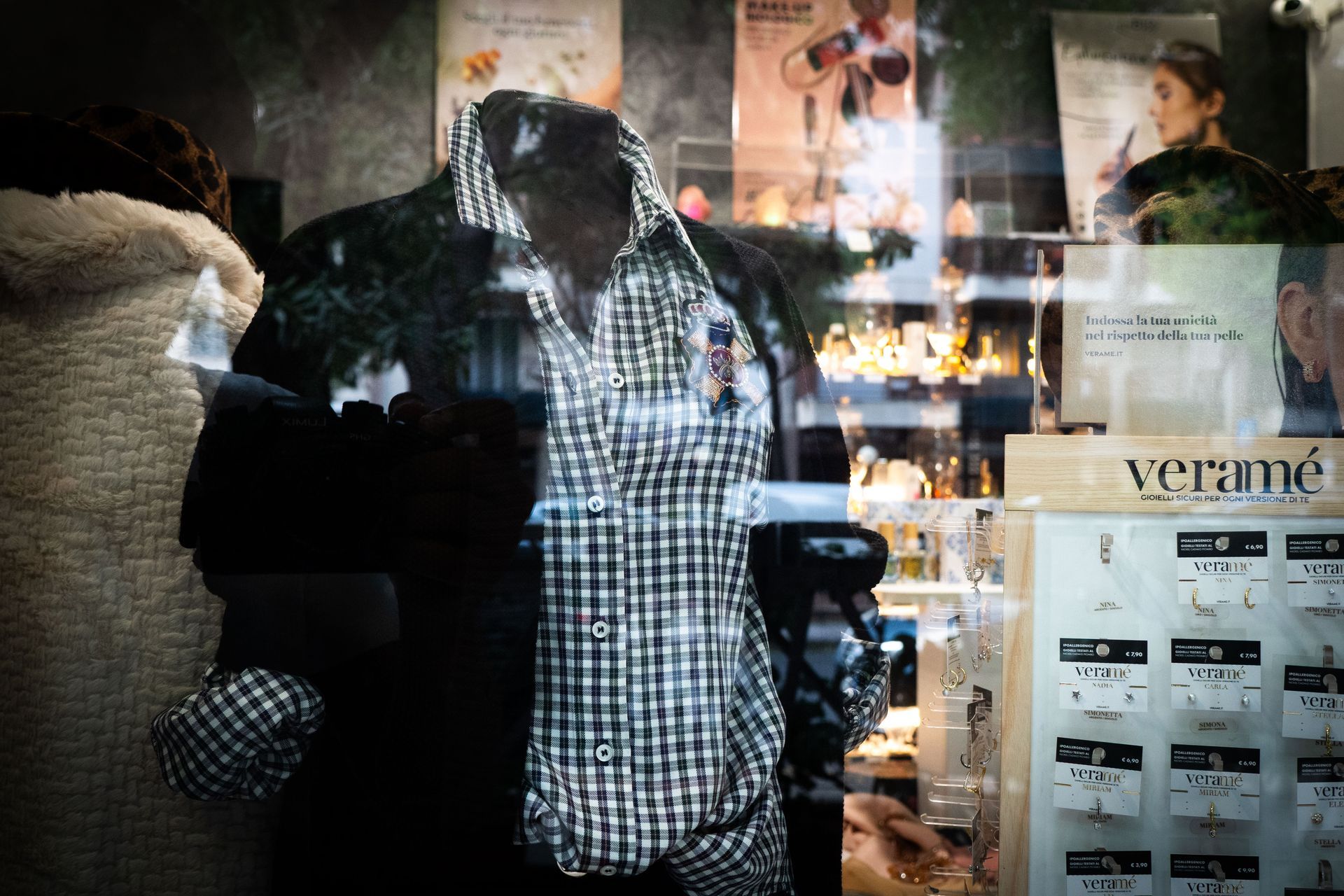 Manichino in vetrina con camicia a quadri e blazer nero. Sono visibili i riflessi del negozio.