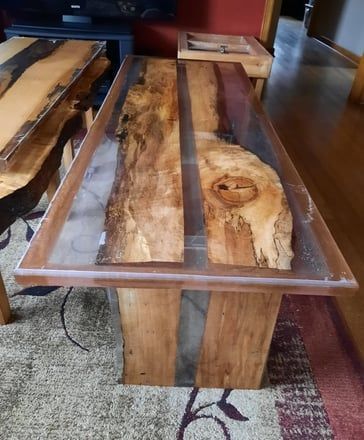 Live edge wood coffee table with clear resin inlay on a wood base, indoor setting.