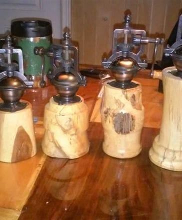 Four wooden pepper grinders with metal mechanisms, sitting on a glossy wooden table.
