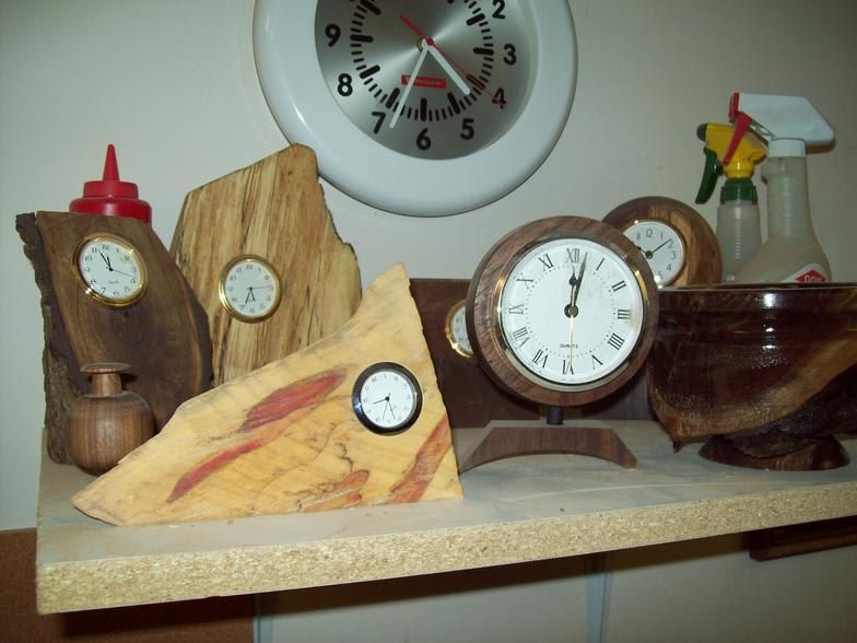 Wooden clocks of various shapes and sizes on a shelf, with a wall clock in the background.