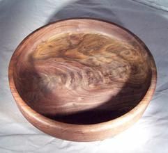 Wooden bowl, brown with swirls, sitting on a white surface.
