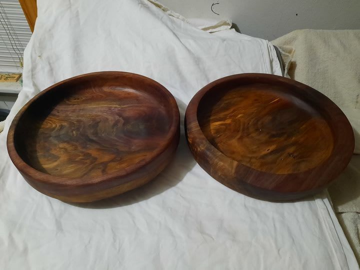 Two wooden bowls with rich brown and swirling grain patterns on a white cloth surface.