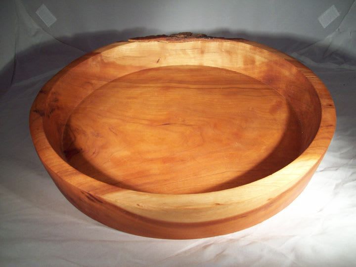 Wooden bowl, light brown with darker interior and smooth texture, sitting on a white surface.