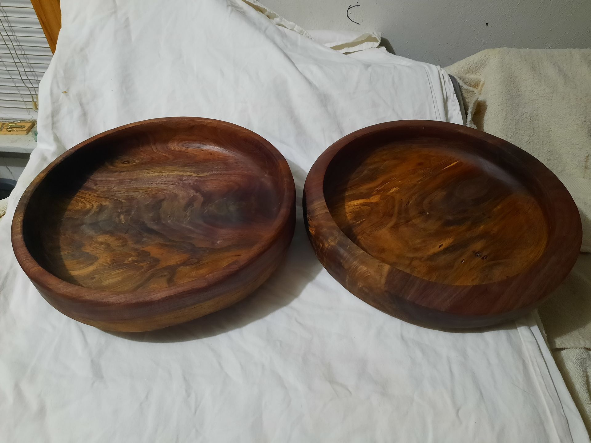 Two wooden bowls with rich brown tones sit side-by-side on a white surface.