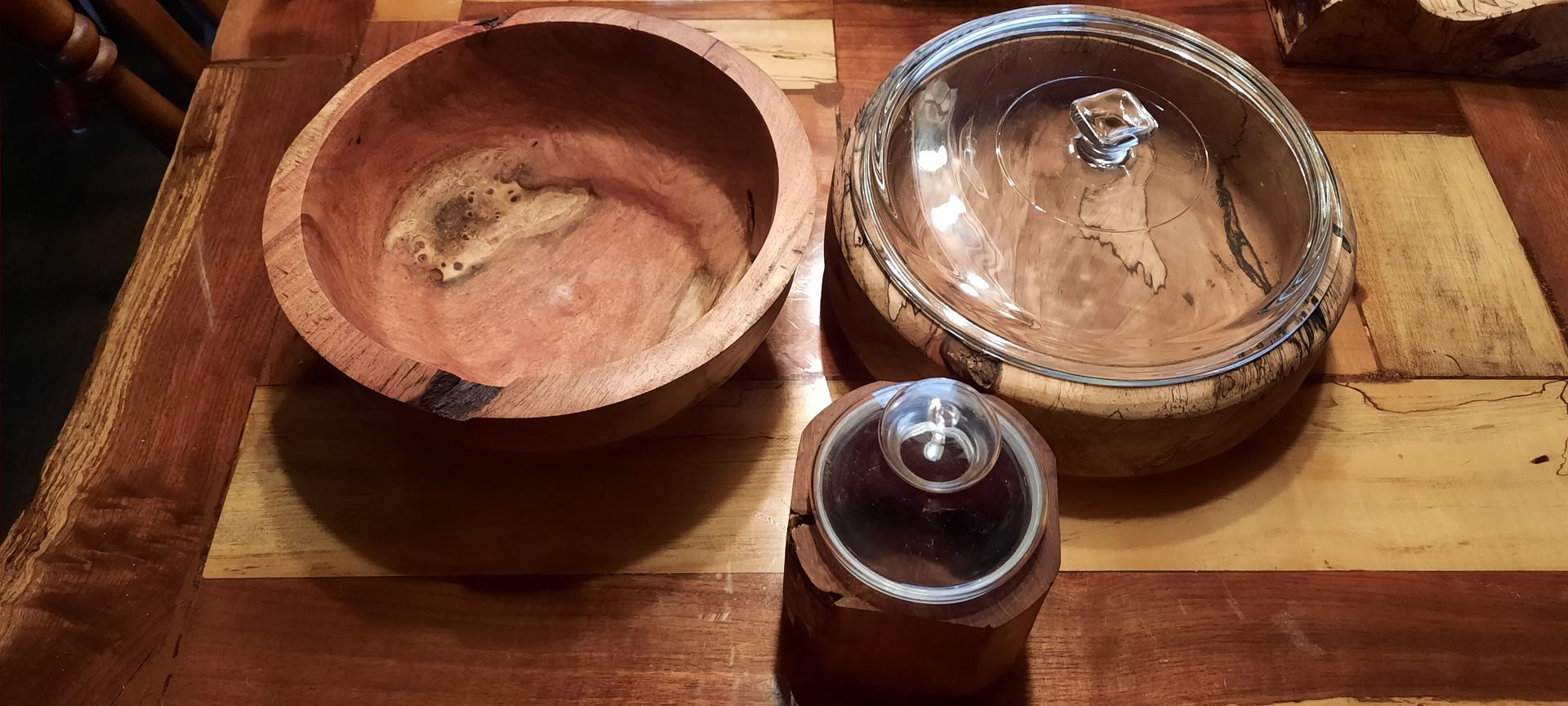 Three wooden bowls on a wooden table, one with a glass lid.