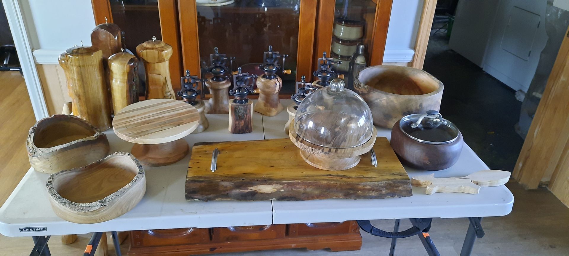 A collection of wooden art pieces on a white folding table, featuring bowls, vases, and decorative objects.
