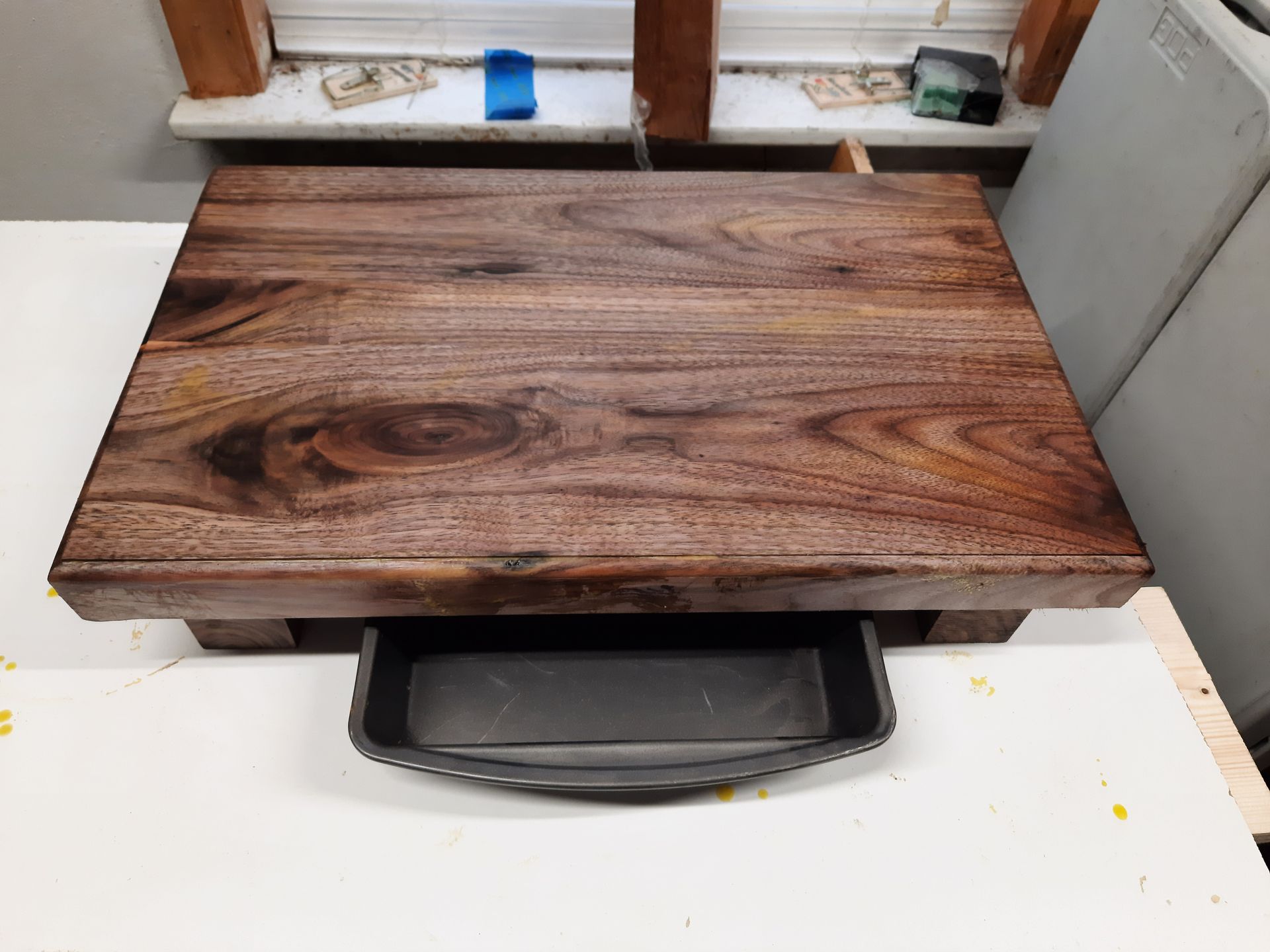 Wooden table with built-in drawer, on a white surface, by a window.