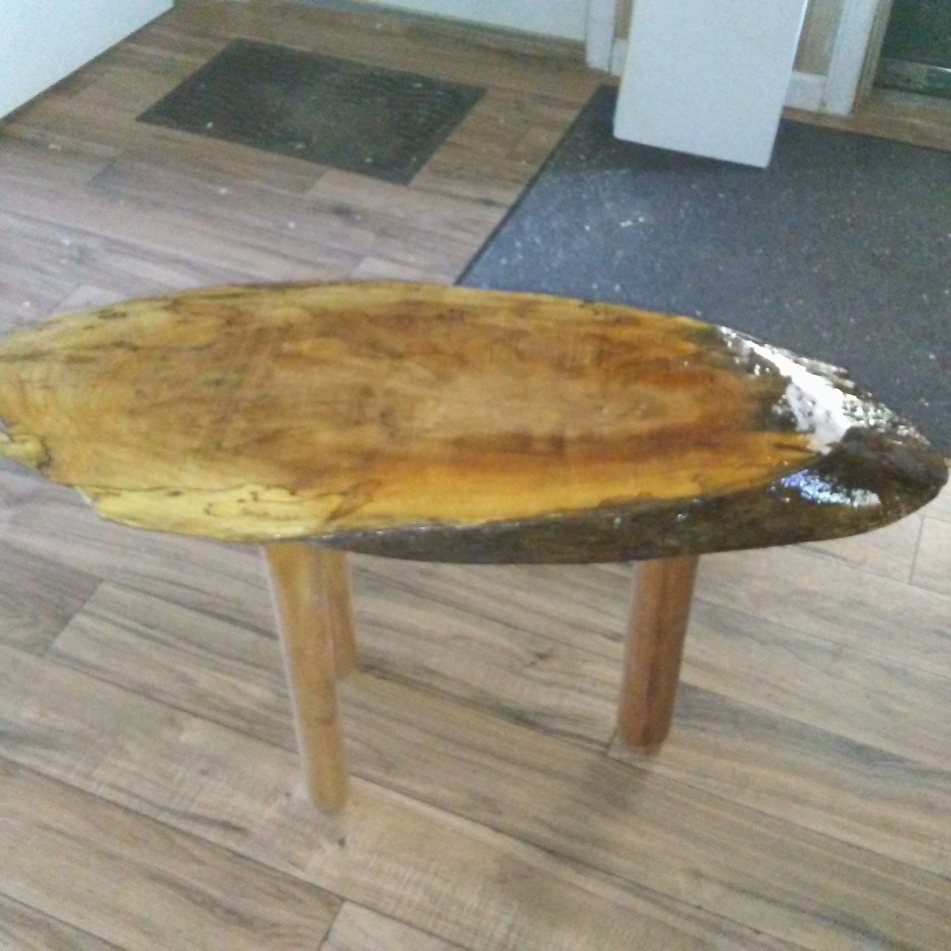 Wooden oval-shaped coffee table with three light-colored legs, set on a hardwood floor.