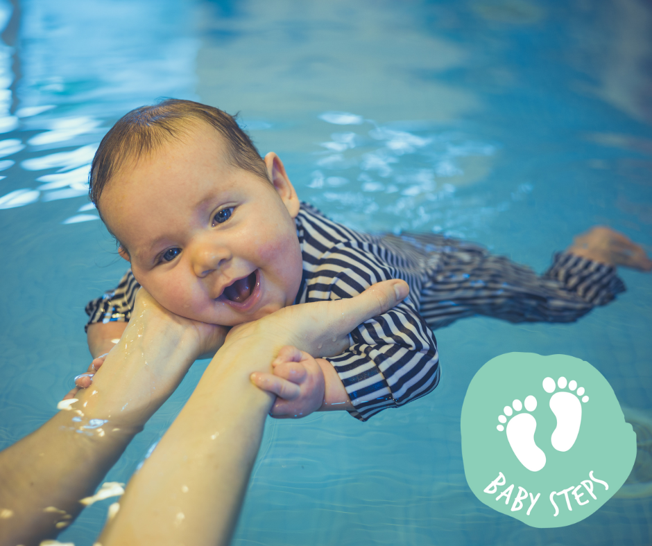 Baby in blue swim shirt, held by an adult in pool, laughing while reaching for toy.
