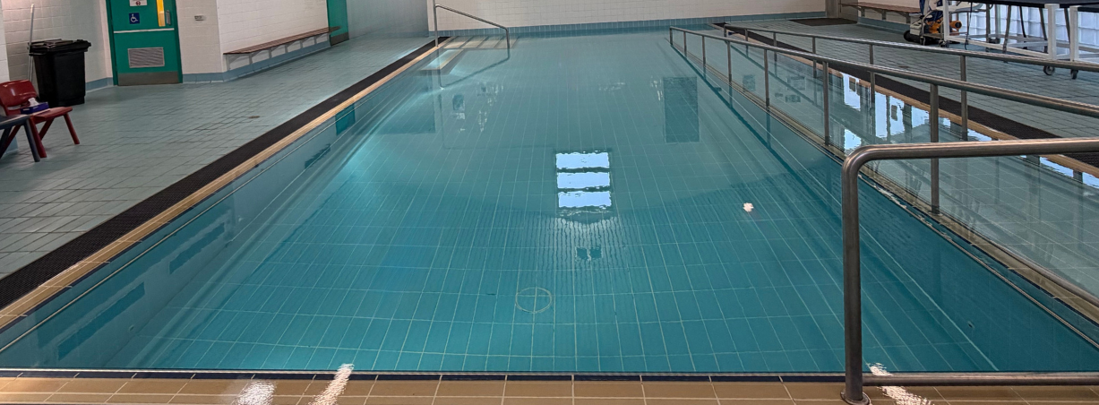 Indoor swimming pool with blue water and stainless steel handrails.