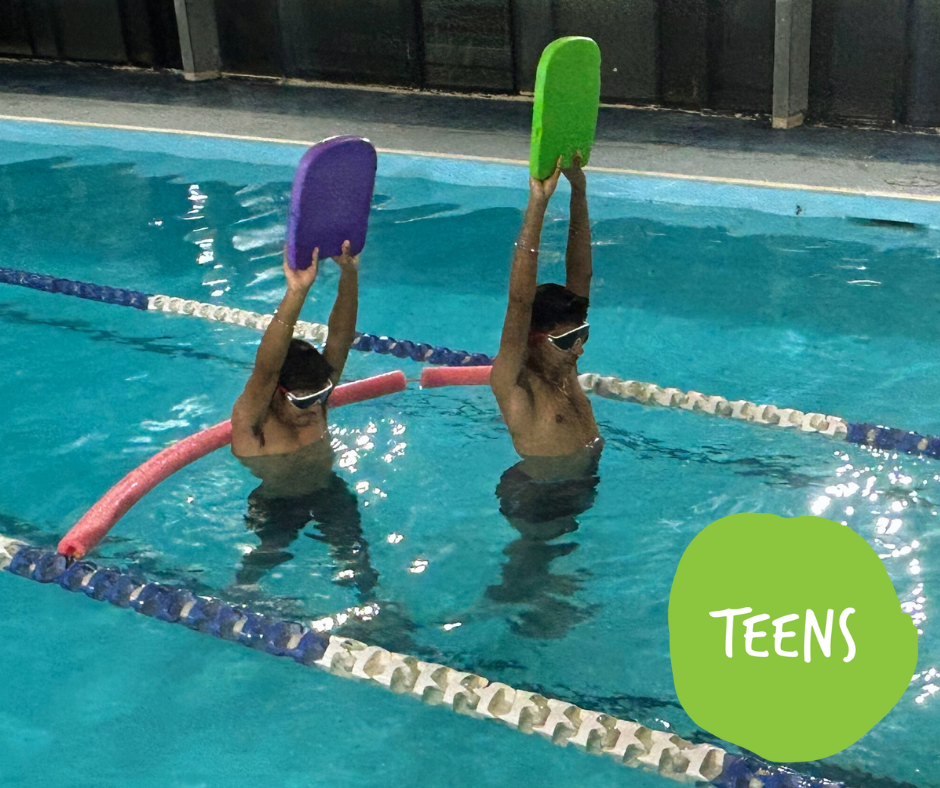 Woman in green shirt holding a girl in a pool. Girl smiles and wears goggles. Both are in blue water.