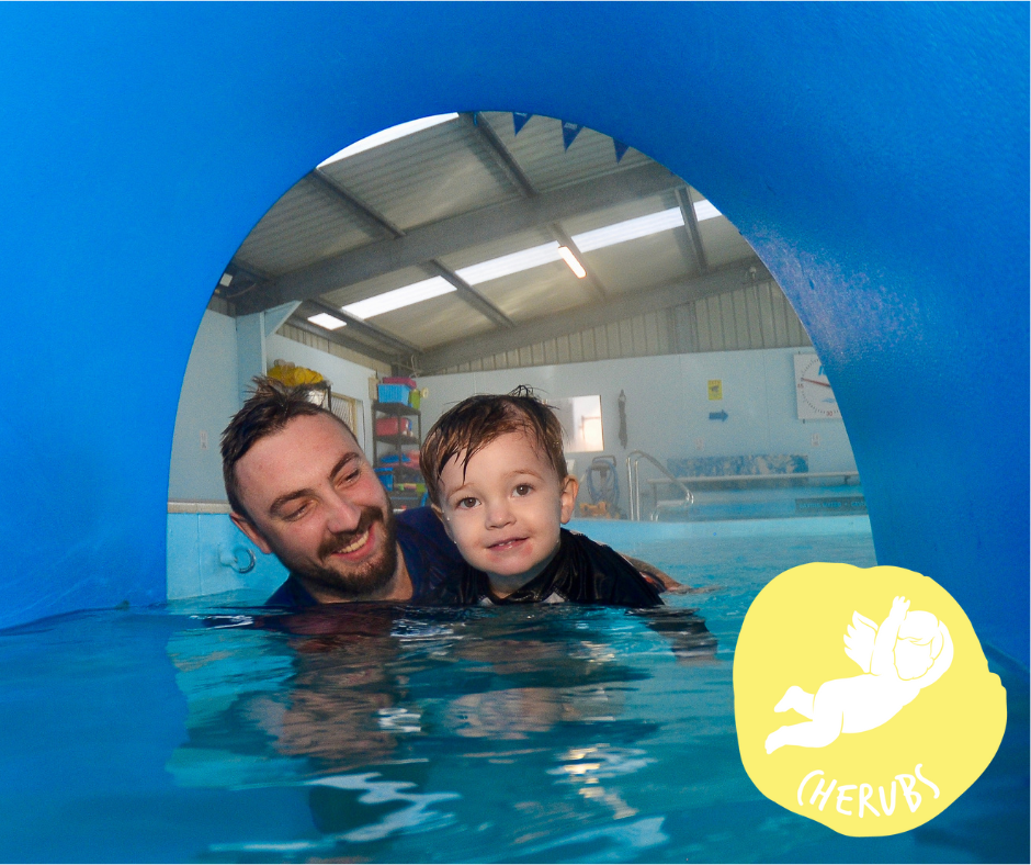Boy underwater in a pool, arms outstretched, wearing colorful swim trunks, with bubbles surrounding him.