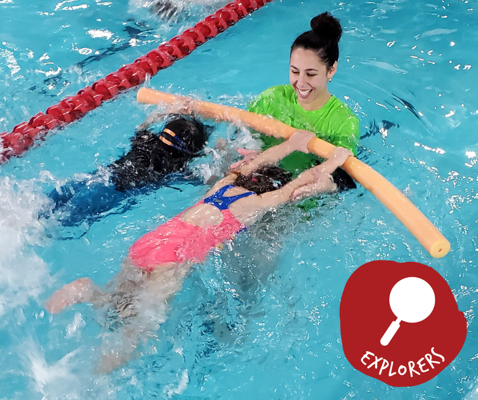Woman in green shirt holding a girl in a pool. Girl smiles and wears goggles. Both are in blue water.