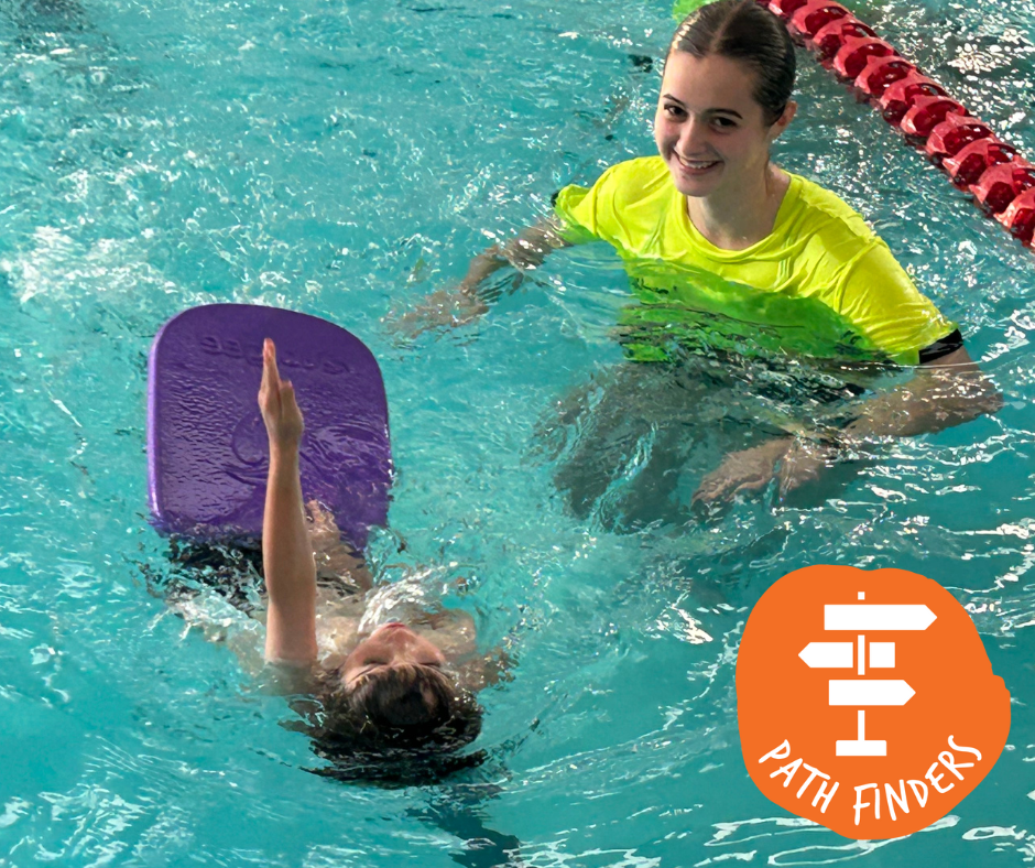 Three people in a pool. Two are looking at a child wearing goggles, who is also in the water, being coached by an instructor.