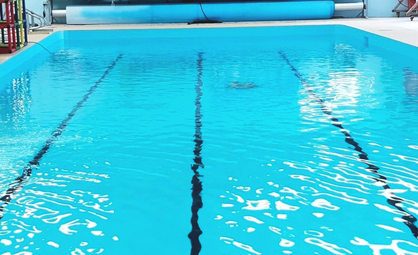 Woman in a swimming cap and goggles in a pool, holding onto a lane rope.