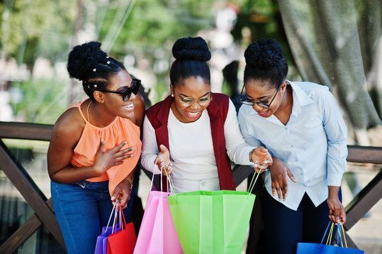 Three women are standing next to each other looking at shopping bags.