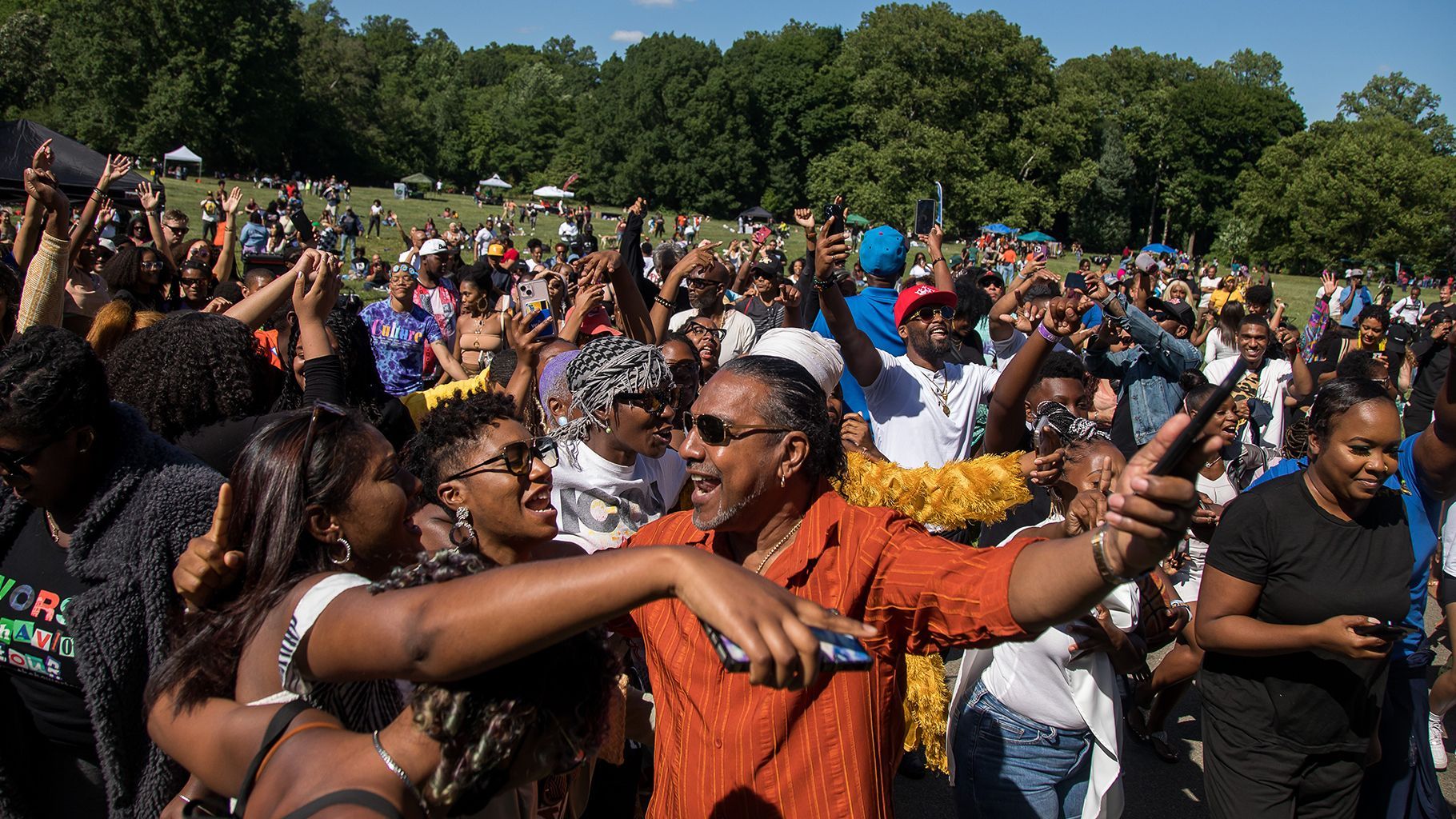 A crowd of people are gathered in a park and one man is taking a selfie