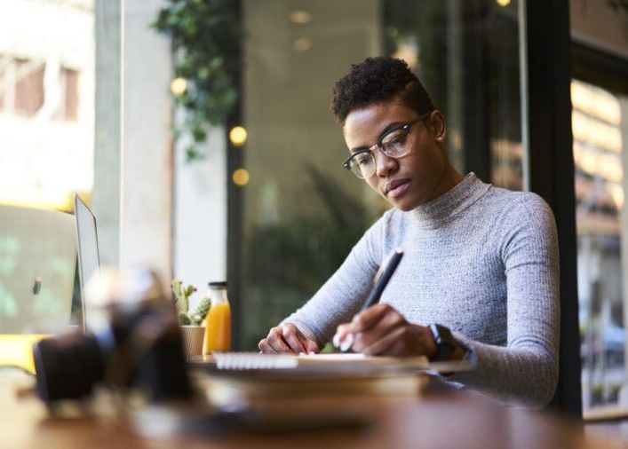 A woman is sitting at a table writing in a notebook.