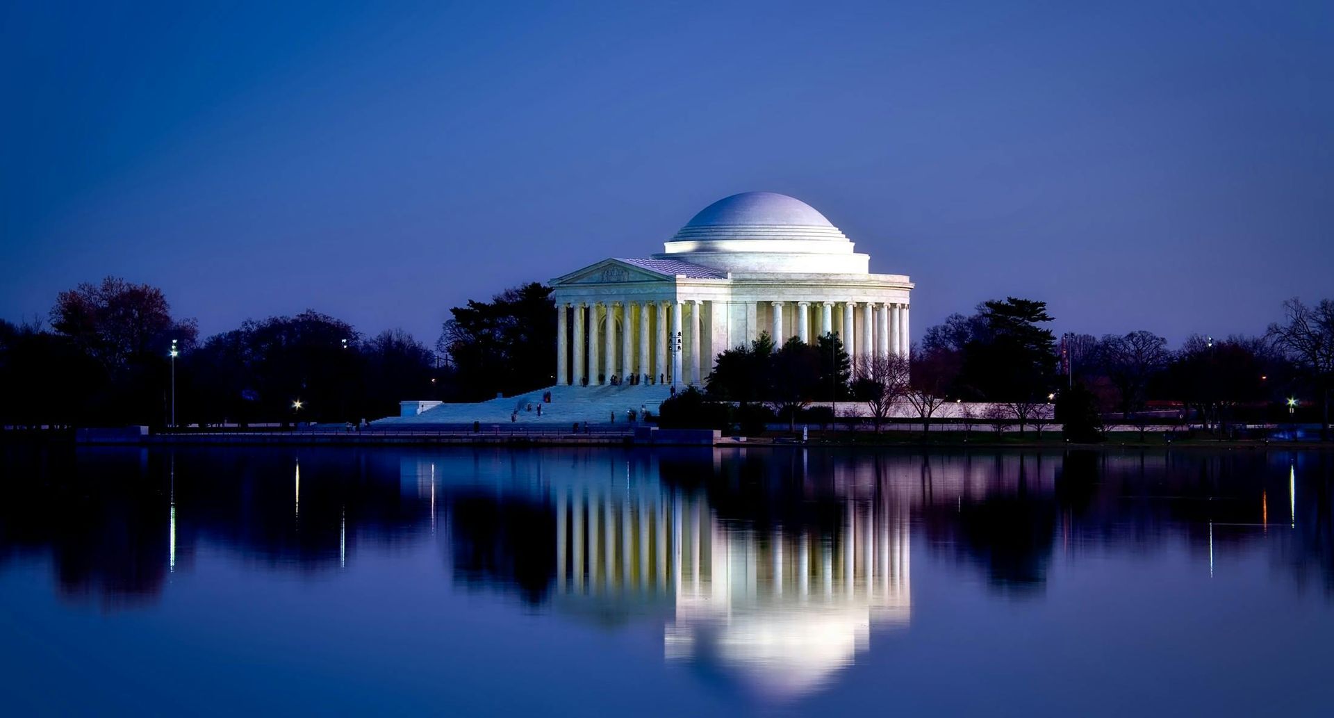 The washington monument is lit up at night and reflected in the water