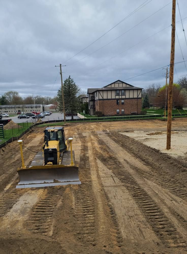 Construction site with a bulldozer grading muddy ground near a brick building under cloudy skies